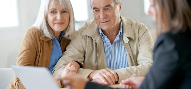 A retiree couple in a meeting with a professional. They are all looking at a laptop screen